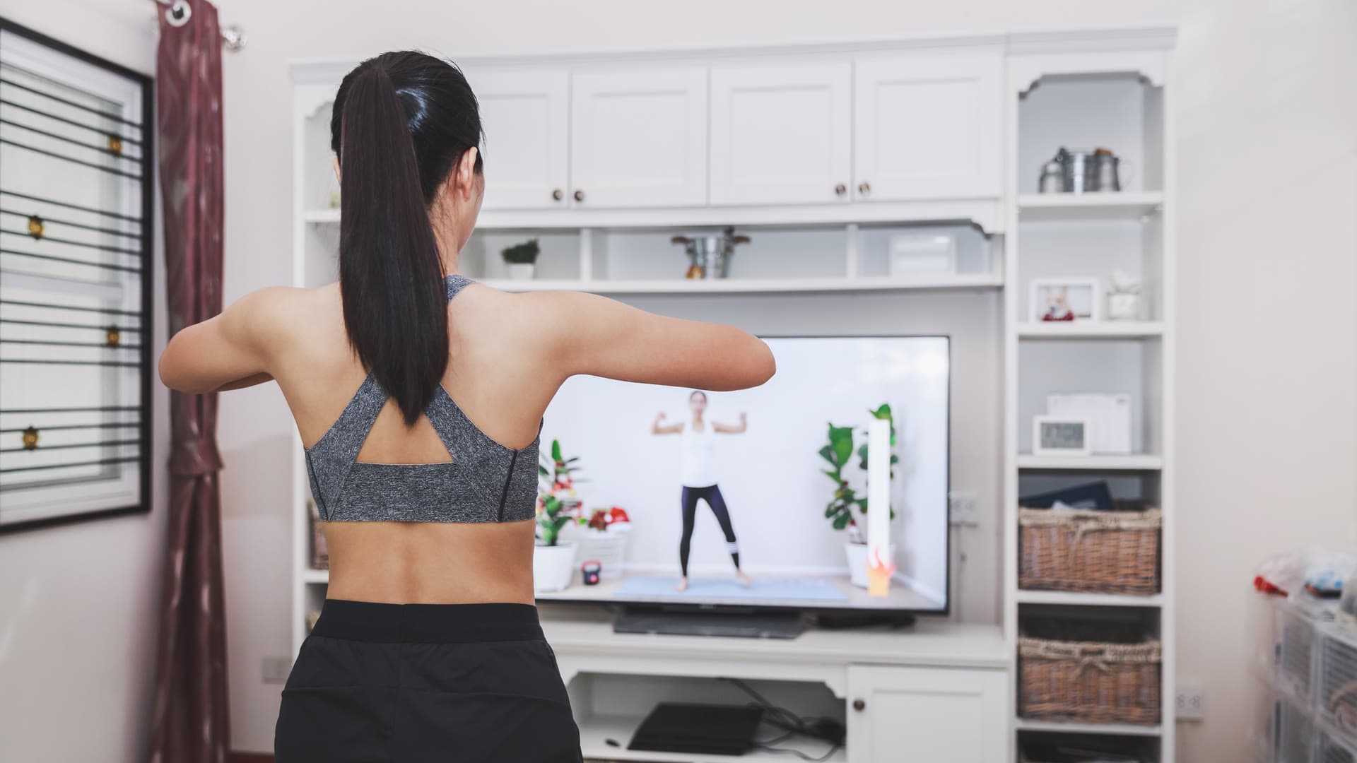 Danseuse qui s'échauffe bras tendus devant sa télévision, dans son salon